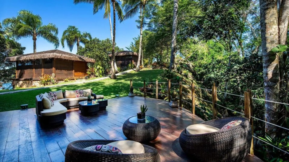 a wooden deck with wicker furniture and a small hut in the background