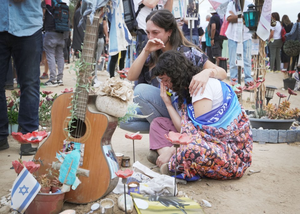 Two women cry as they look at a tribute to one of the victims