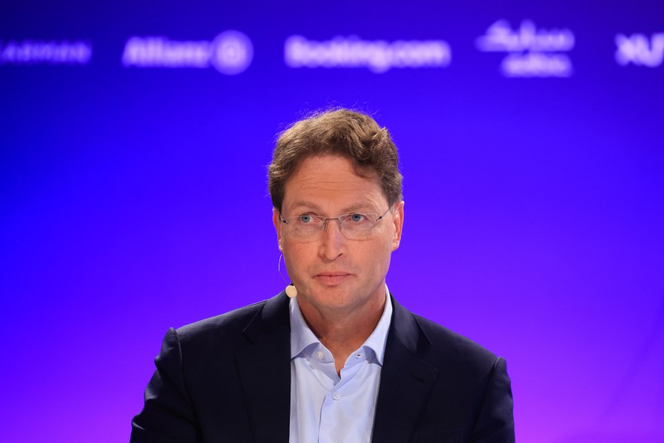 a man wearing glasses and a suit stands in front of a blue background that says booking.com