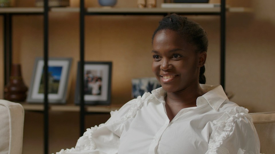 a woman in a white shirt smiles while sitting on a couch