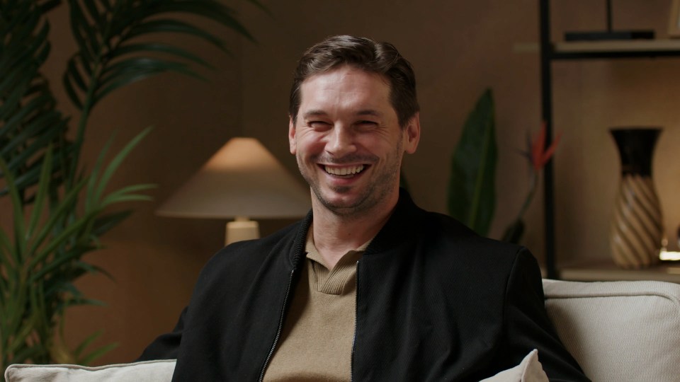 a man in a black jacket is smiling while sitting on a couch