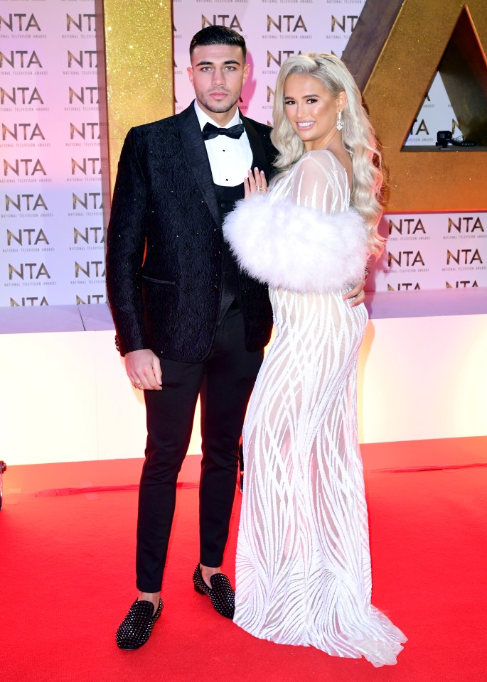 a man in a tuxedo and a woman in a white dress pose on a red carpet