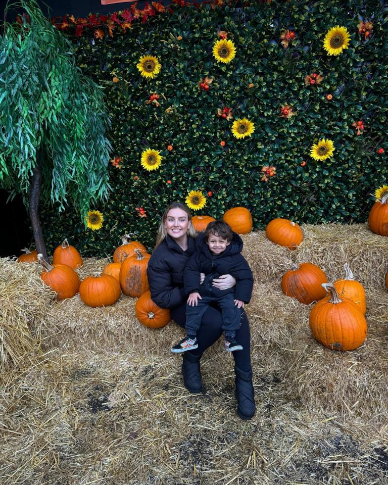 a woman holding a child in front of a wall of pumpkins