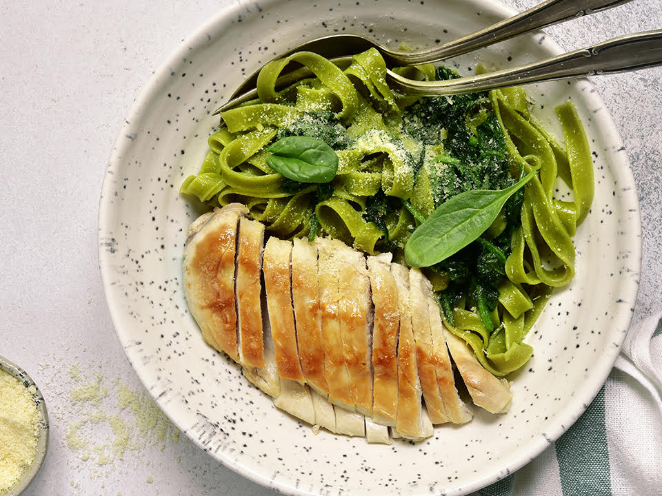 a plate of pasta with chicken and spinach on a table