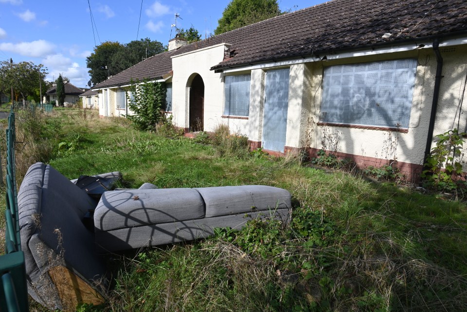 a couch sits in the grass in front of an abandoned house