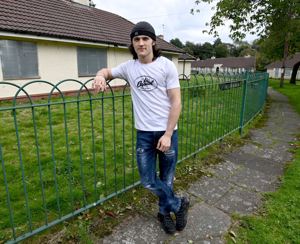 a man leaning against a fence wearing a shirt that says original