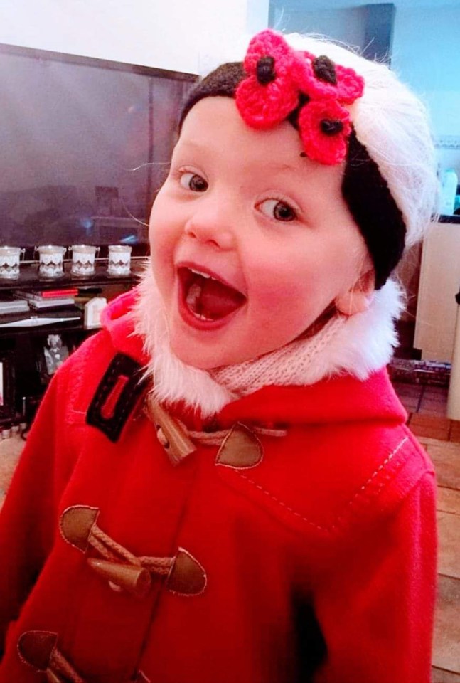 a little girl wearing a red coat and a headband with a poppy on it