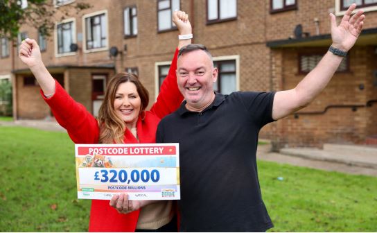 a man and a woman are holding a cheque in front of a building .