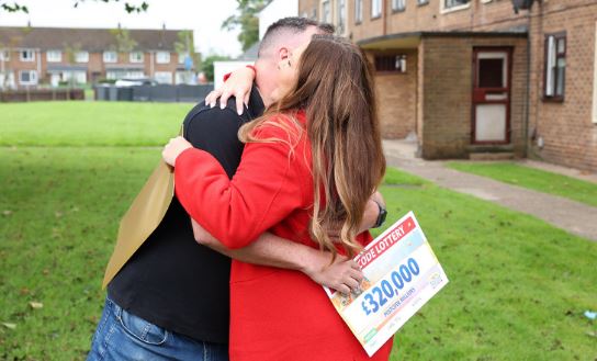 a man is hugging a woman who is holding a lottery ticket .