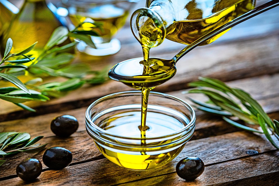 olive oil is being poured into a glass bowl