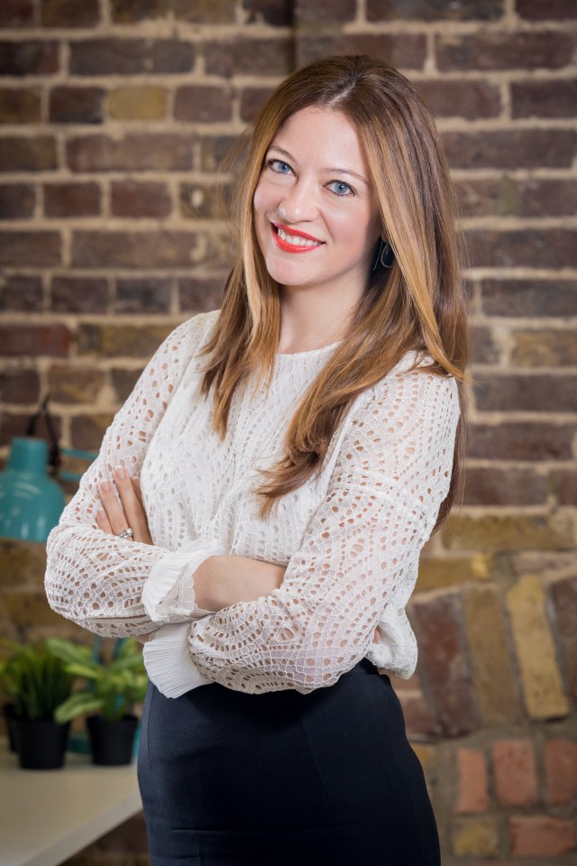 a woman with her arms crossed is smiling in front of a brick wall