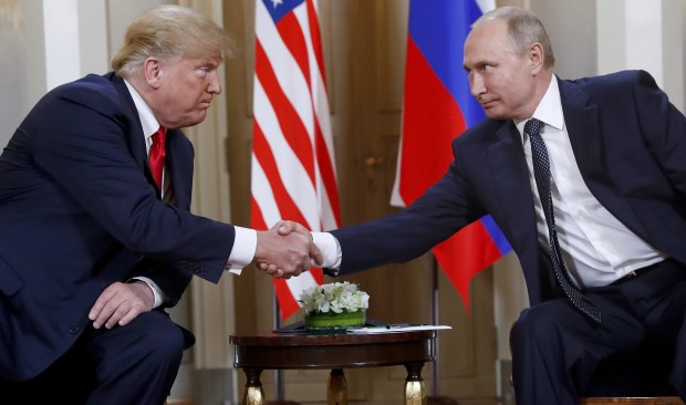 two men in suits shake hands in front of flags