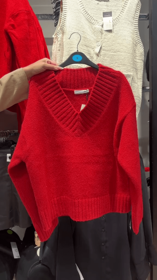 a red sweater is hanging on a hanger in a store