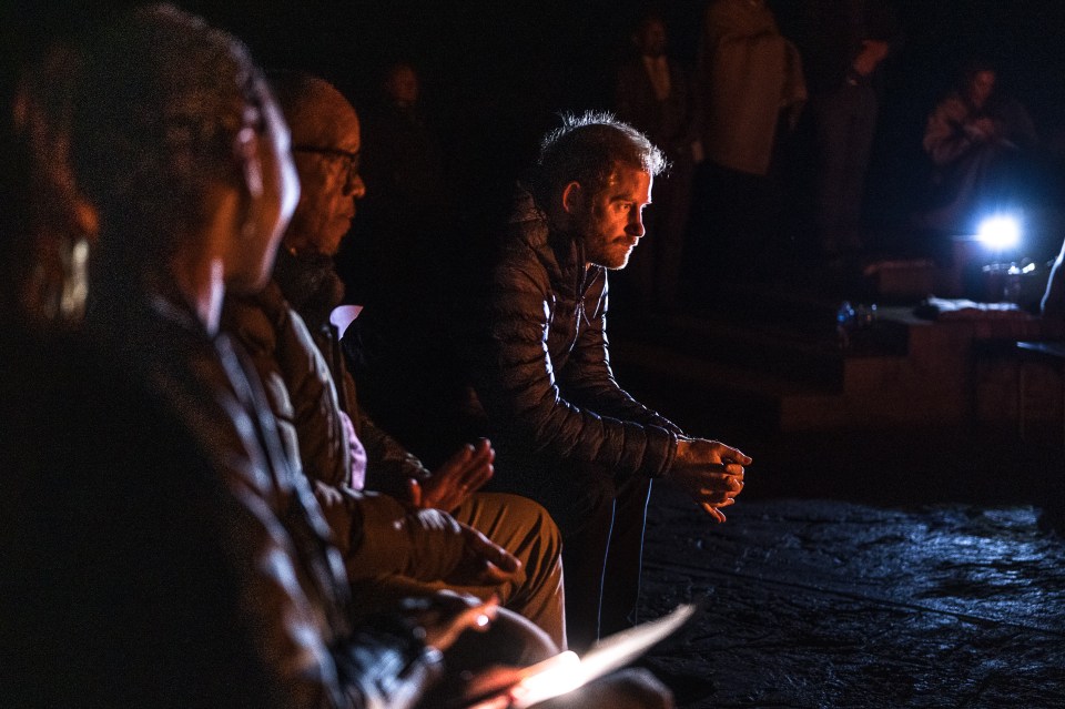 a man in a black jacket sits in a dark room