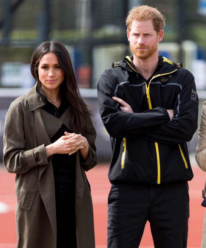 harry and meghan stand next to each other with their arms crossed