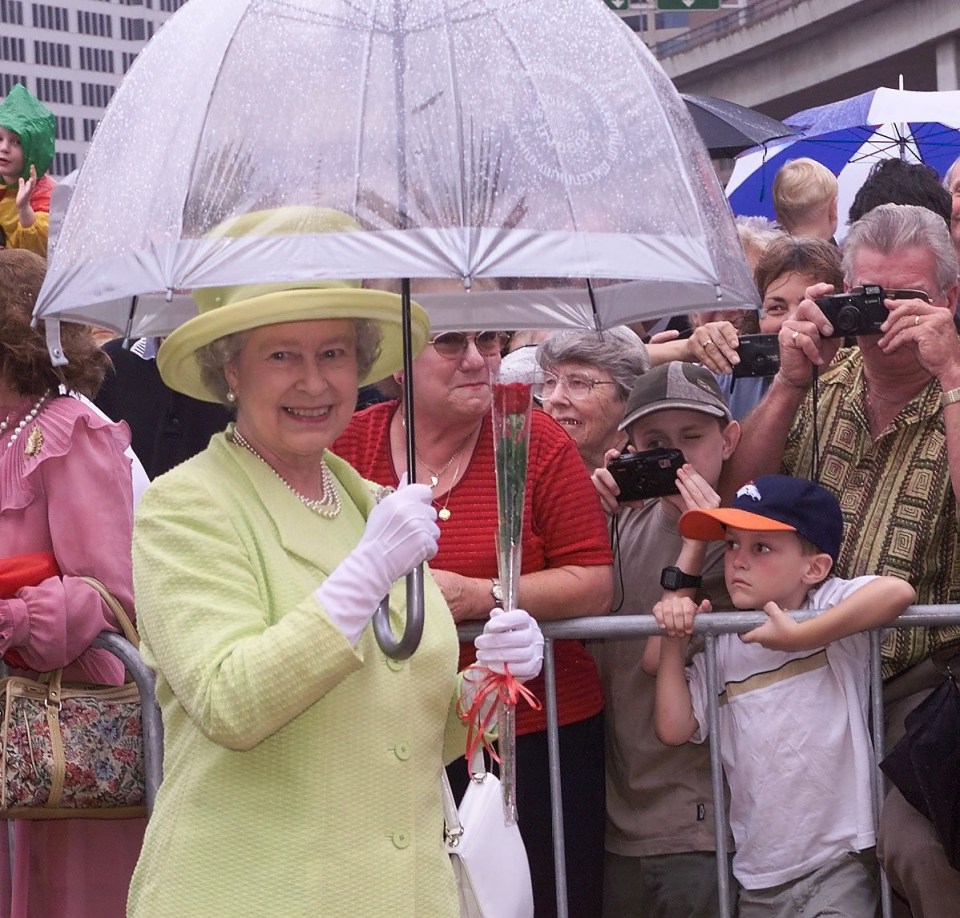 queen elizabeth is holding an umbrella in front of a crowd