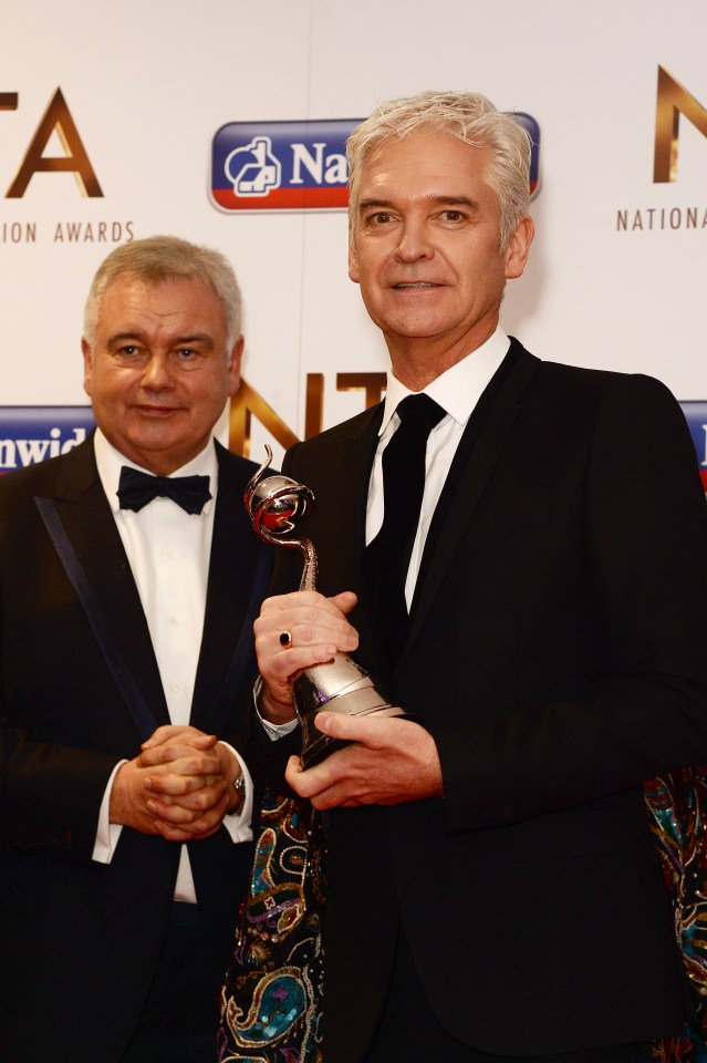 a man in a tuxedo holds a trophy next to another man in a tuxedo