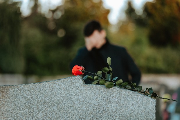 a man stands behind a gravestone with a red rose on it