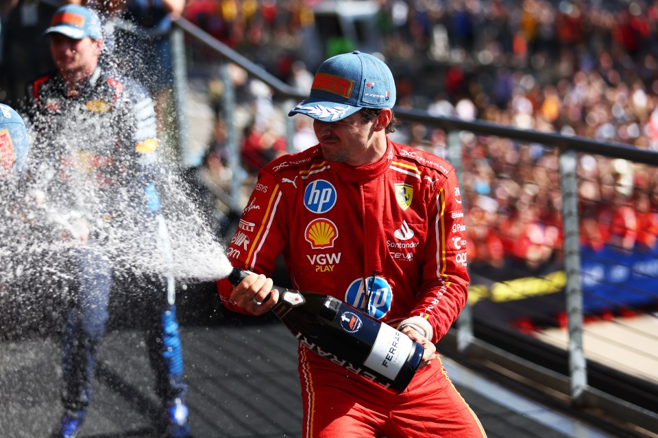 a man in a red ferrari uniform is holding a bottle of champagne