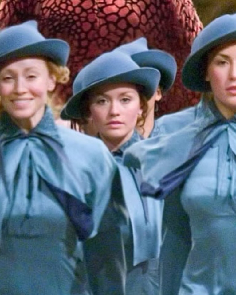 a group of women wearing blue hats and dresses are standing next to each other .