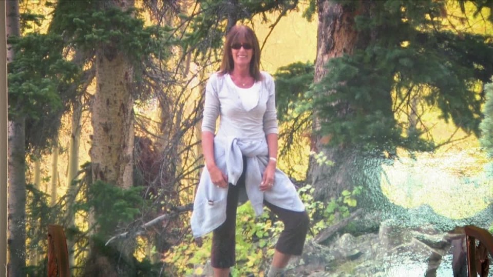 a woman wearing sunglasses stands in front of a forest