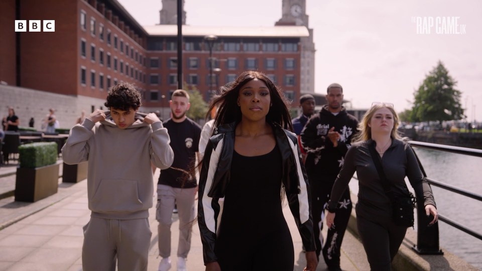 a group of people are walking down a sidewalk with the bbc logo in the background