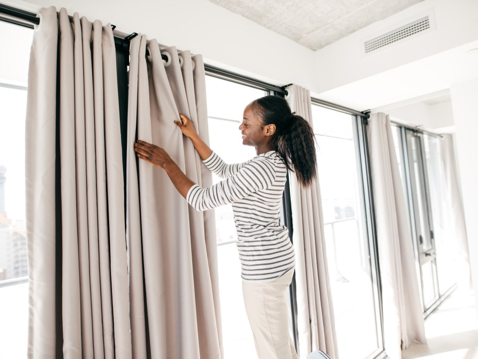 a woman in a striped shirt is hanging curtains on a window