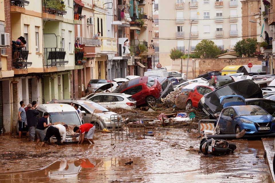 Residents look at cars piled up after being swept away by floods in Valencia today