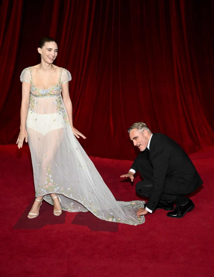 a man helps a woman with her dress on the red carpet