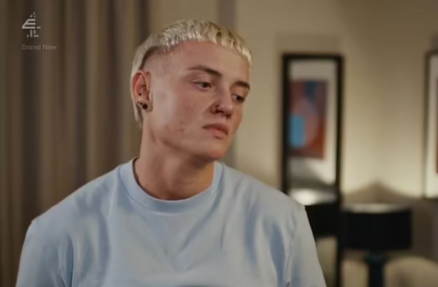 a young man with blonde hair and earrings is sitting in a living room .