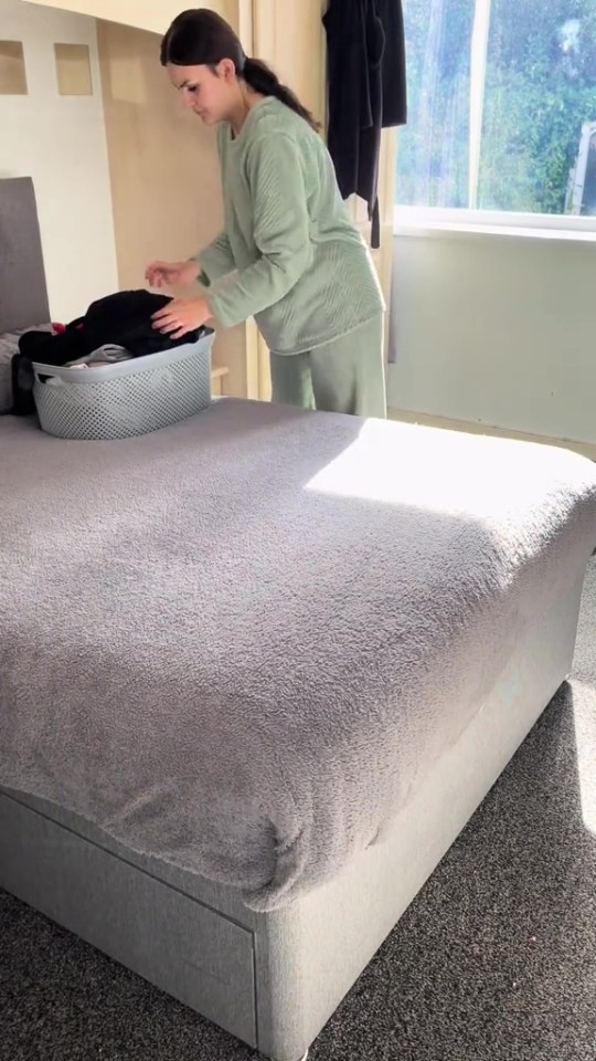 a woman is putting clothes in a basket on a bed