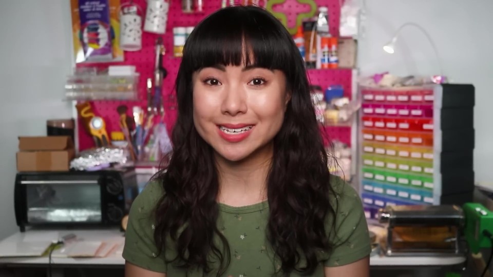 a woman in a green shirt is smiling in front of a pink wall