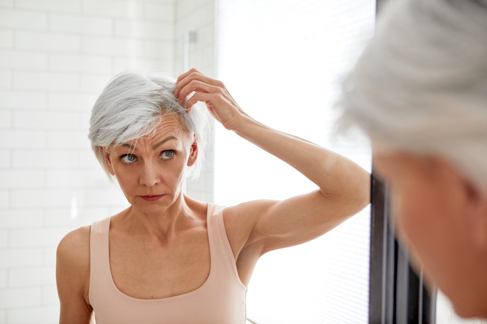 a woman looks at her gray hair in the mirror