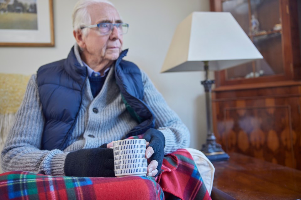 an elderly man sits on a couch holding a cup of coffee