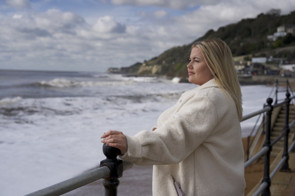 a woman in a white coat looks out over the ocean