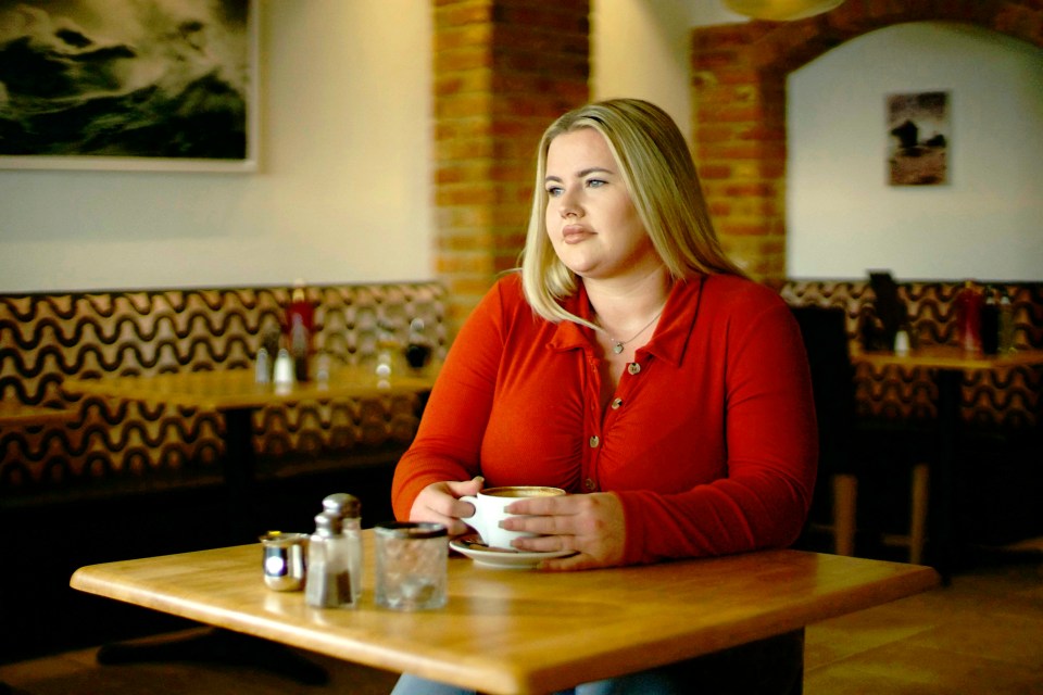 a woman sits at a table holding a cup of coffee