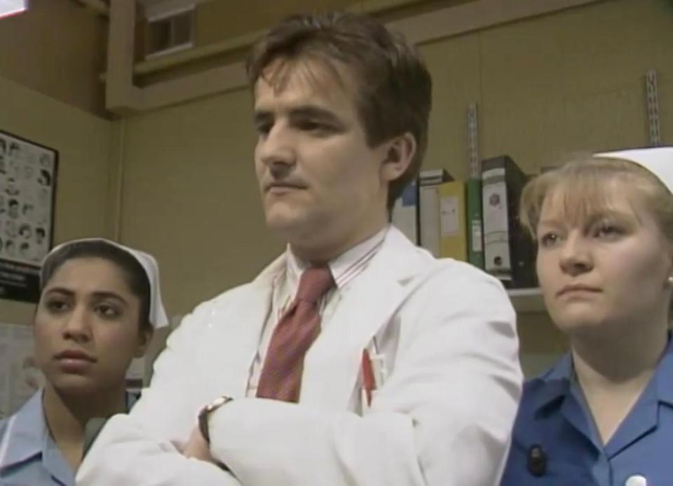 a man in a lab coat and tie stands between two nurses