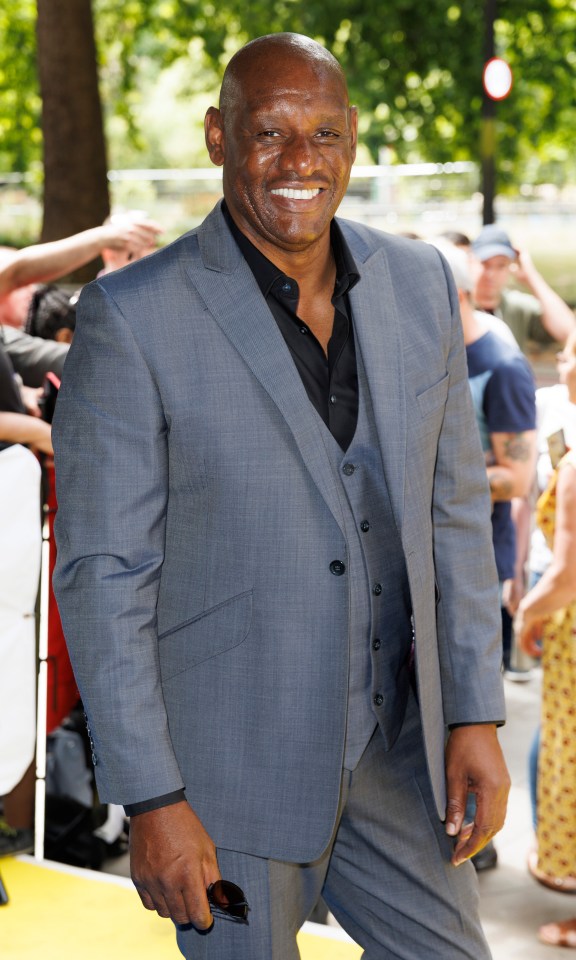 a man in a grey suit and black shirt smiles for the camera