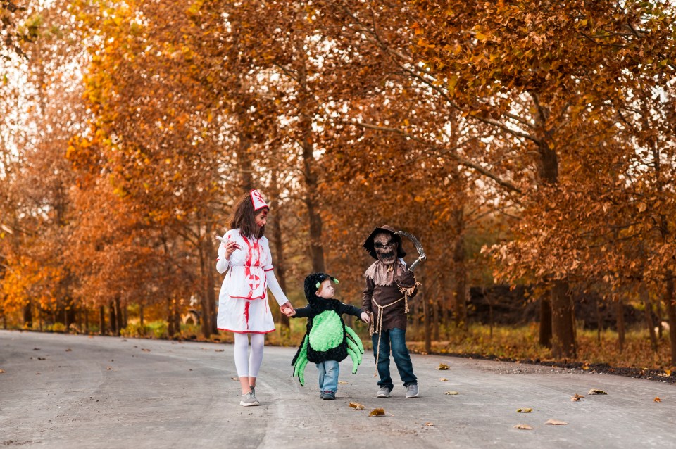 a woman and two children in halloween costumes are walking down a road