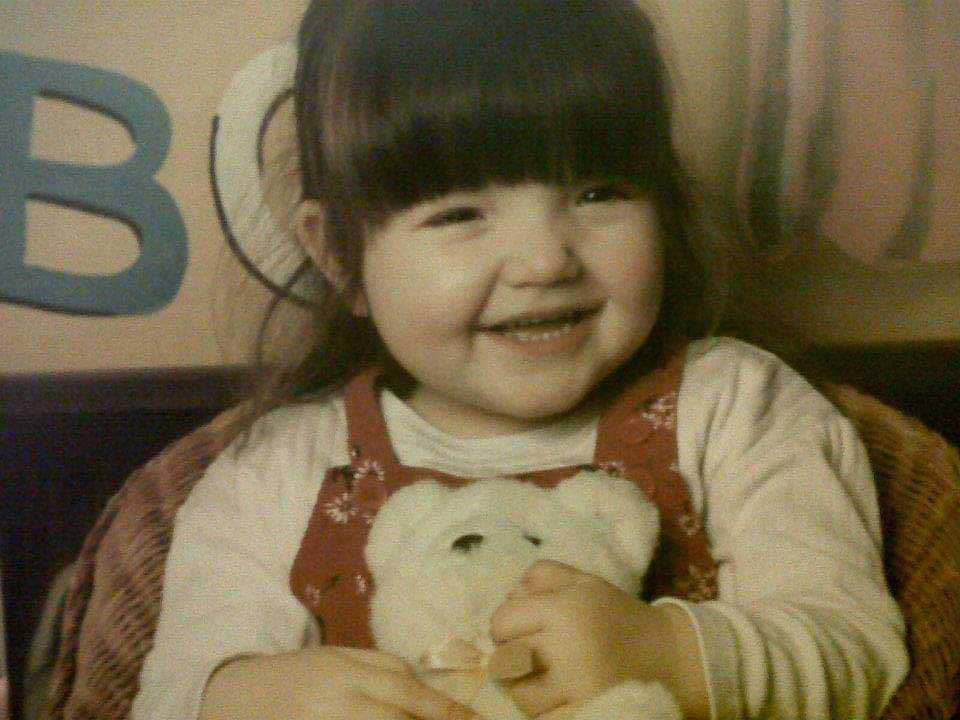 a little girl holding a teddy bear in front of a wall with the letter b on it