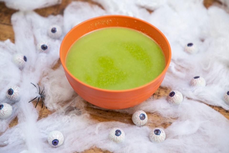 a bowl of green liquid surrounded by fake eyes and spiders