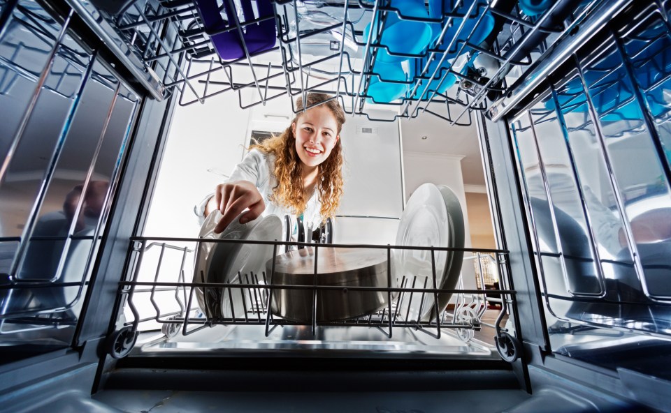 a woman is putting dishes in a dishwasher and smiling