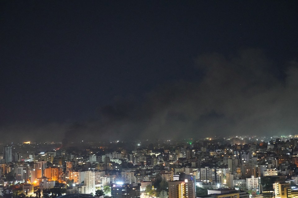 an aerial view of a city at night with smoke coming out of the buildings