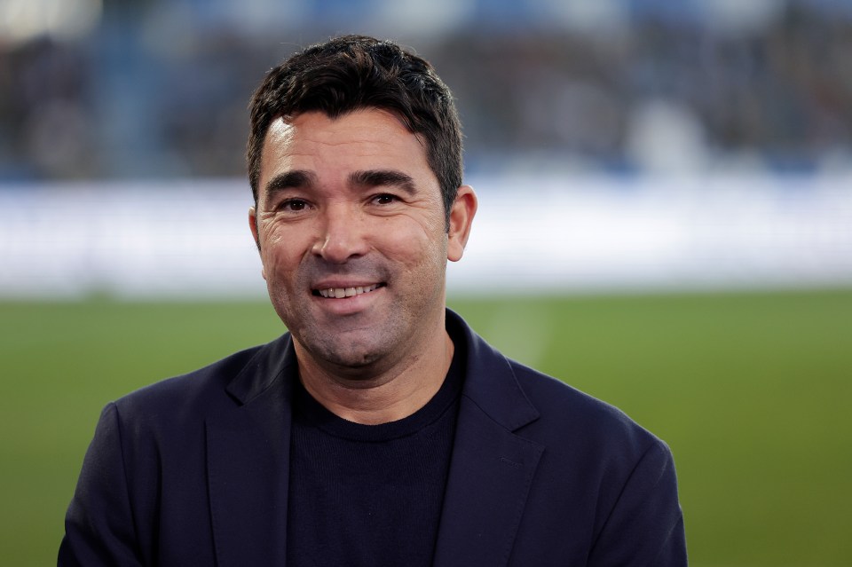 a man in a suit smiles in front of a soccer field