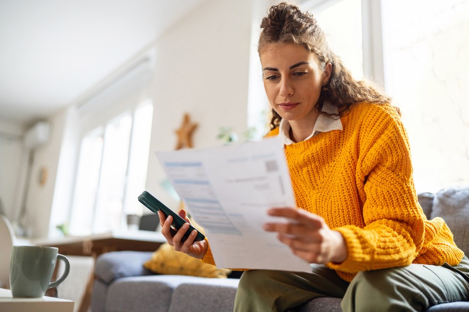 a woman in a yellow sweater sits on a couch holding a cell phone and a piece of paper