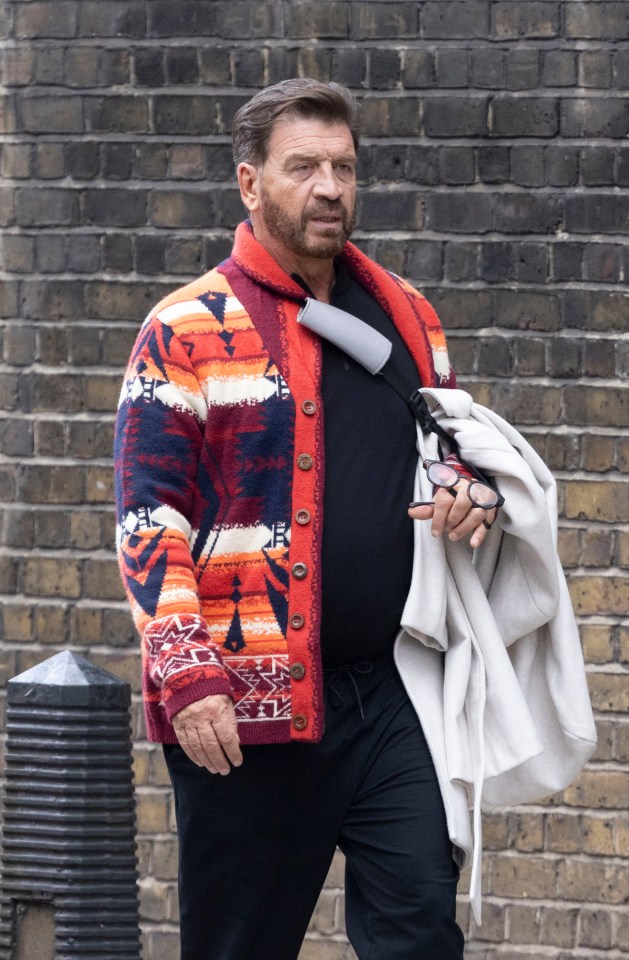 a man wearing a colorful sweater is standing in front of a brick wall