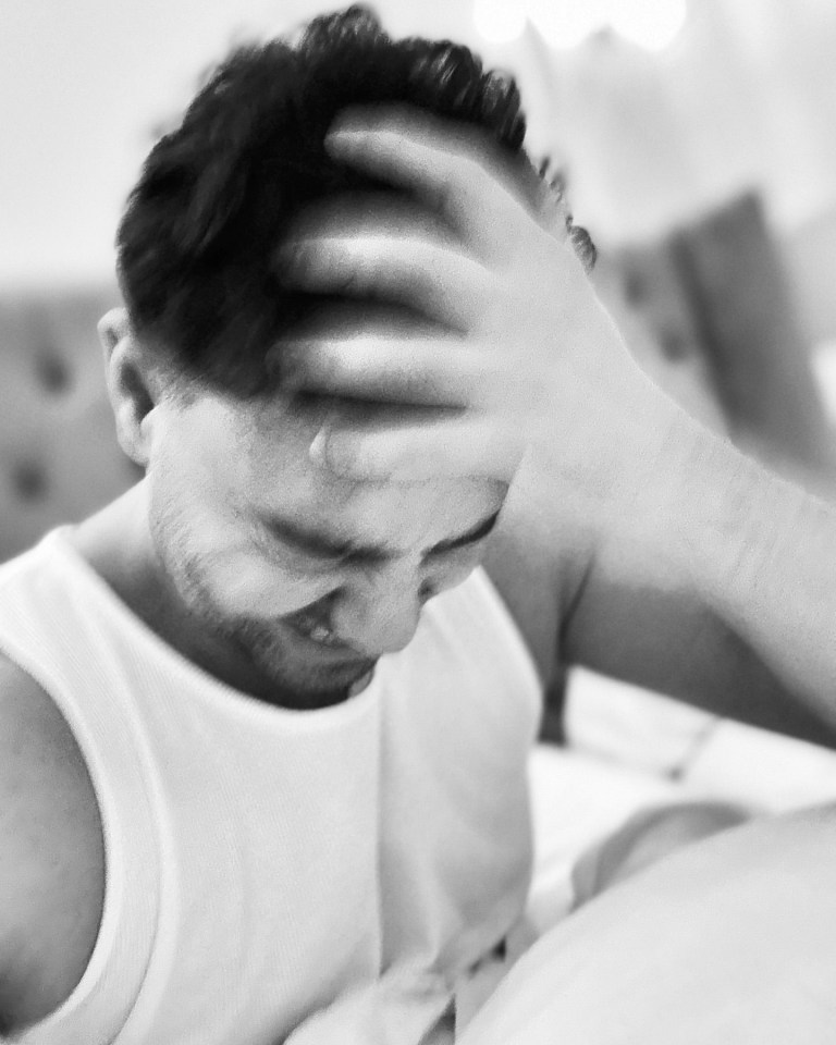 a man in a white tank top is covering his face with his hand