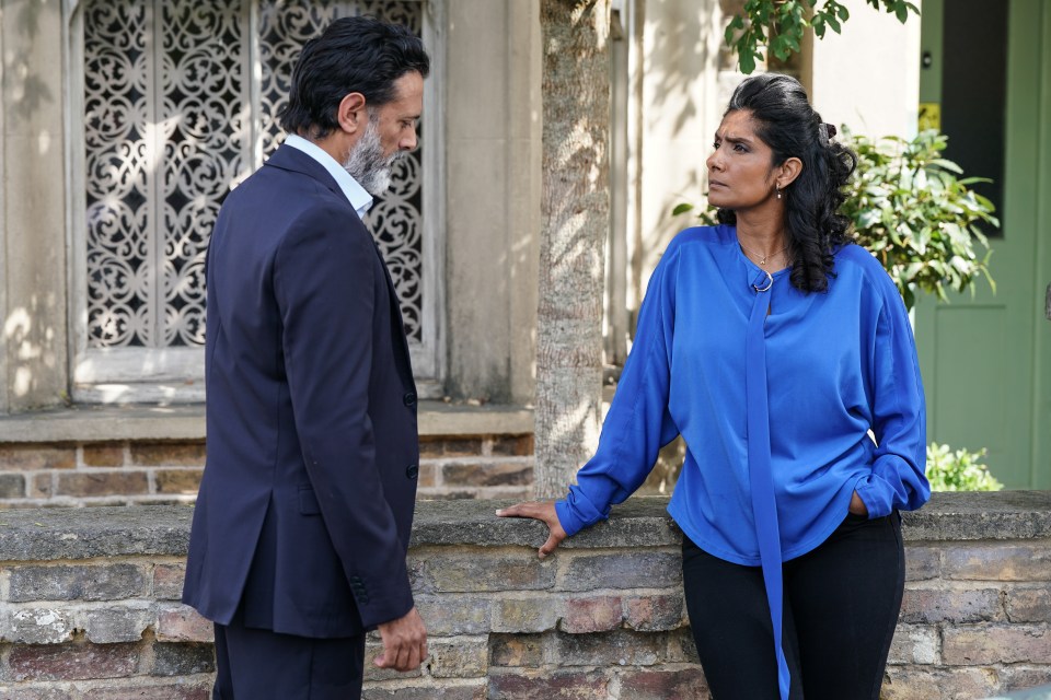 a man in a suit stands next to a woman in a blue shirt