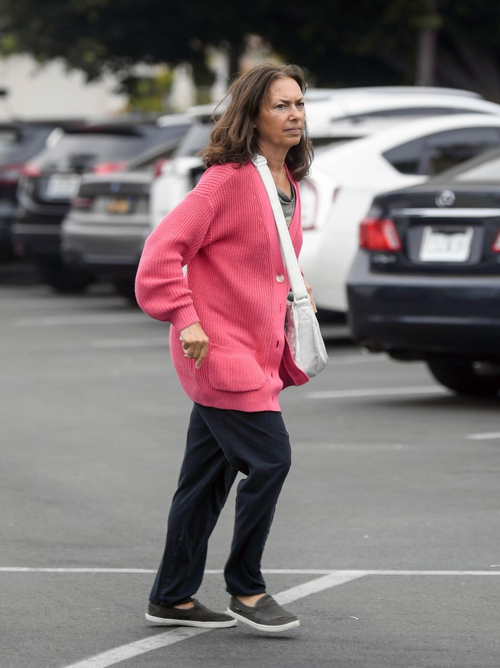 a woman in a pink sweater is walking in a parking lot