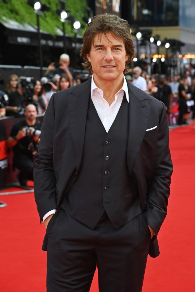 a man in a suit stands on a red carpet with his hands in his pockets